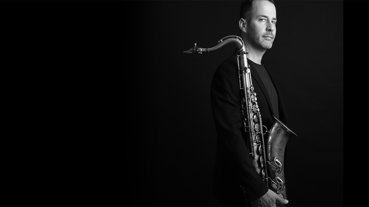 Carson Freeman holding a saxophone in front of black background