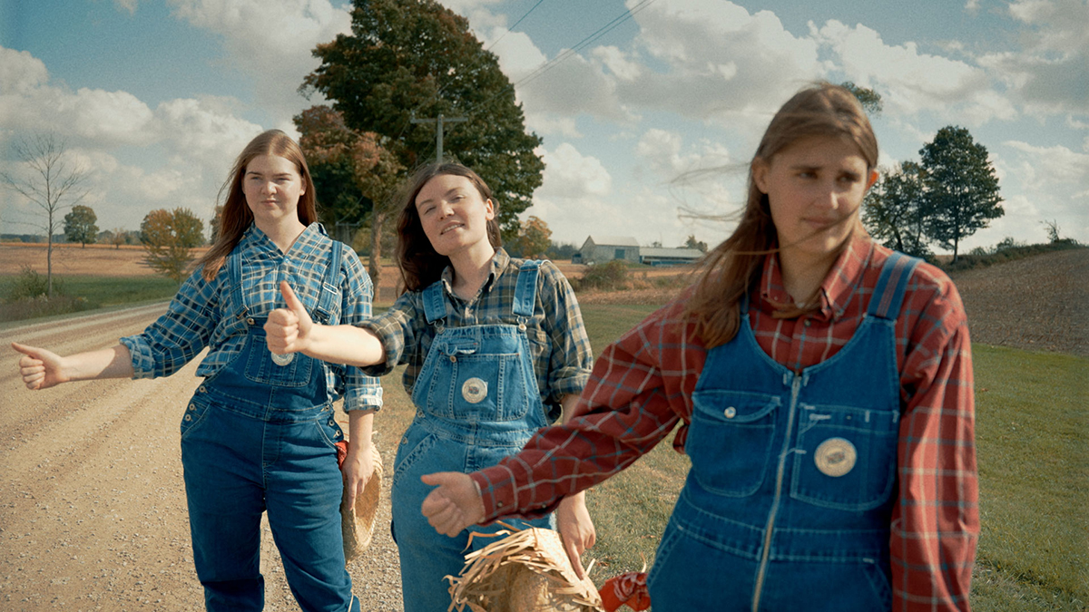 A group of women hitchhiking on the side of a dirt road