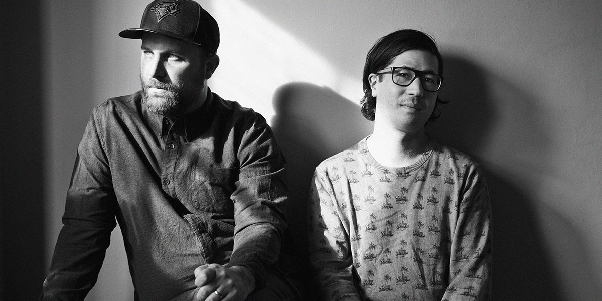 Nobu Adilman and Daveed Goldman posing against a wall.