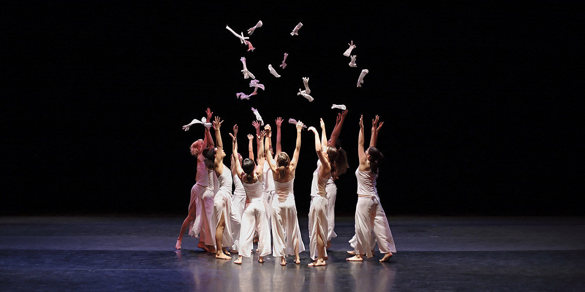 A group of dancers on stage in white dresses.