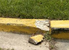 A yellow curb with a large piece of concrete missing 