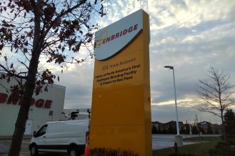 A large yellow sign with the Enbridge logo and address in front of a parking lot.