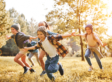 Four kids running through a grassy area in fall clothing.