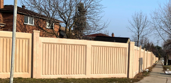 Image of a noise wall along the sidewalk and some houses behind the wall