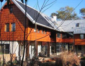 Photo of a two-storey home. The first storey created with white stucco and lots of windows, while the second story has an orange-brown wood siding and grey metal roofing.