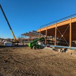 Workers and a telescopic handler at a construction site with a crane.