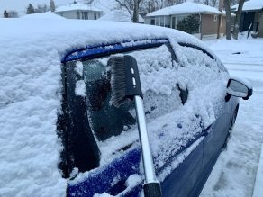 Brushing snow off blue vehicle