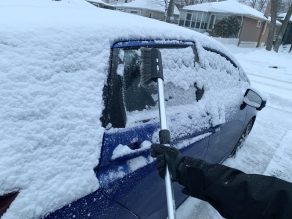 Clearing snow of blue car with black snow brush