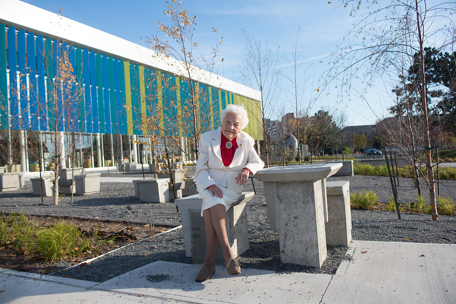 Hazel McCallion, former Mississauga Mayor, sitting on a concrete bench in front of Meadowvale Community Centre.