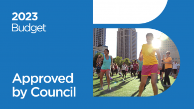 Designed graphic with a blue background and photo of people exercising outside. The graphic also has 2023 Budget as well as Approved by Council written on it