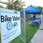 A City staff member standing under a tent to a row of bicycles and a sign that says, Bike Valet.