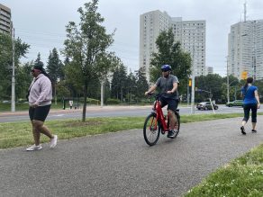 Person riding e-bike with two pedestrians walking on multi-use trail in Mississauga.