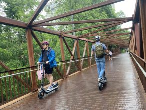 Two people riding e-scooter on multi-use trail across bridge in Mississauga.