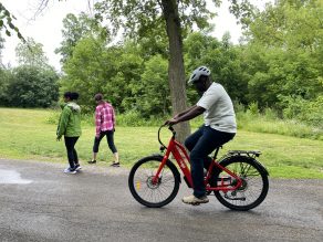 Person riding e-bike on park trail with two pedestrians walking.