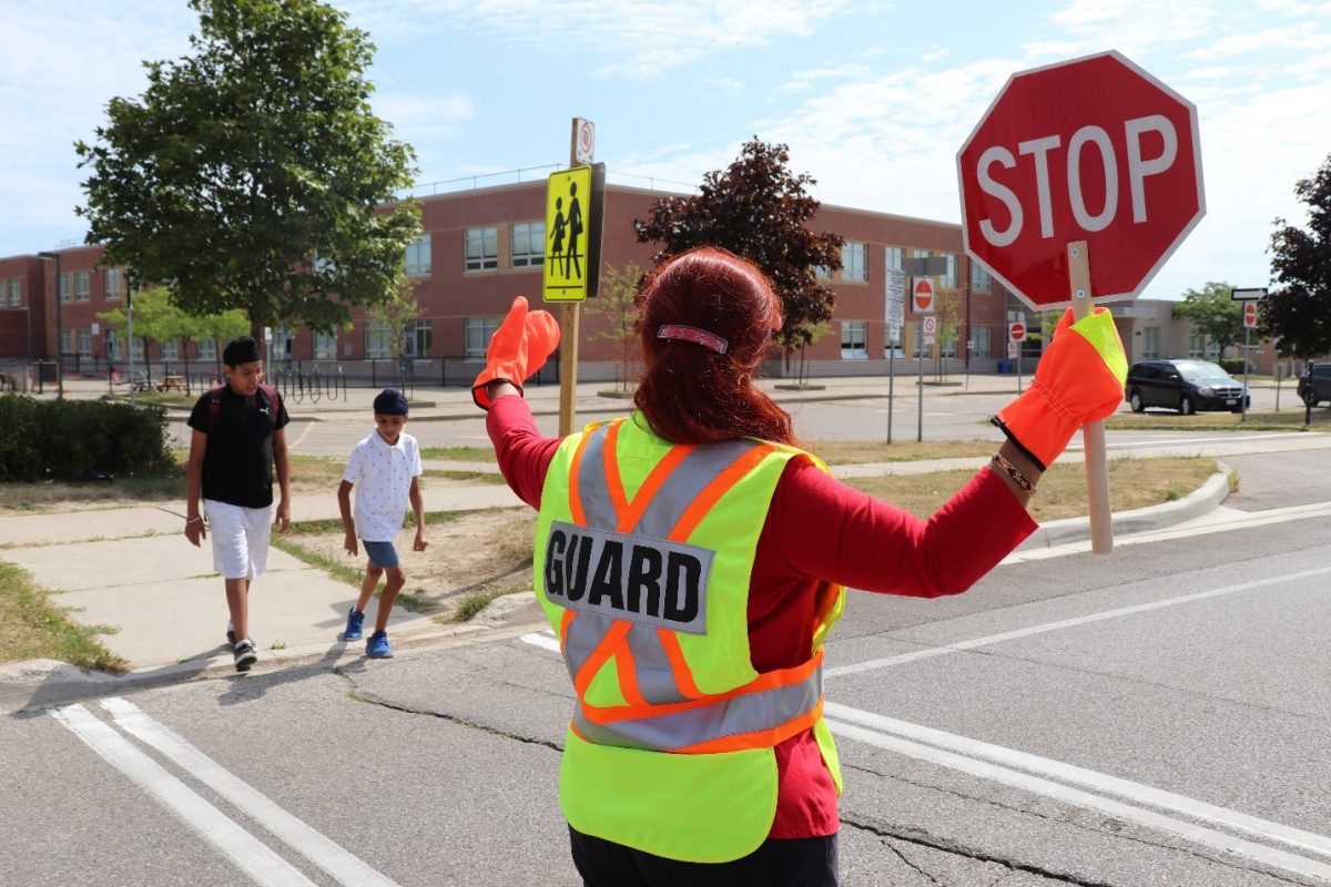 School crossing guard directing pedestrians to cross the street near a school.