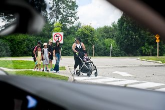 Group of students and parents walking across crosswalk to get to school. This is see from a driver's perspective who has stopped and is waiting for the group to cross.