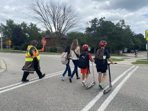 Group of students and parents walking across crosswalk with crossing guard.