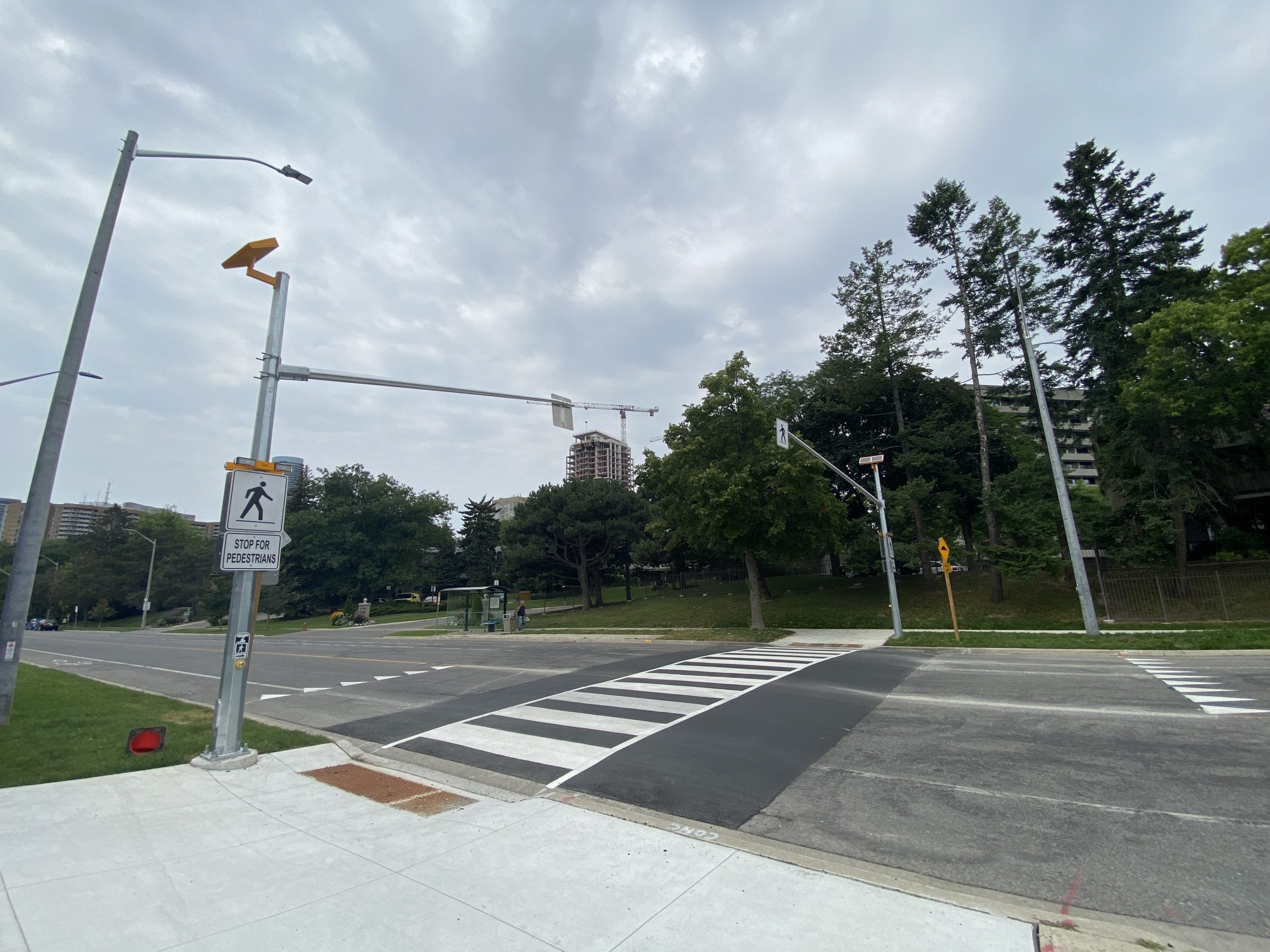 Pedestrian crossover at an intersection marked by white road markings painted on the ground and a stop for pedestrians signage installed on the traffic light pole.