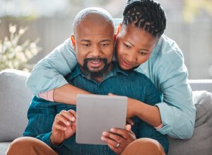 a mature woman hugging her husband while he uses a digital tablet.