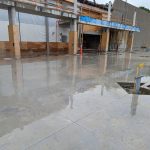 The exterior of a building under construction surrounded by a concrete slab that is slick with water.