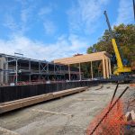 A construction site with a yellow crane and large wood beams on the ground.