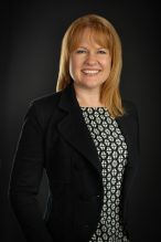 Headshot of Lori Kelly into the new role of Director of Municipal Transition and Integration. She is standing in a business suite in front of a dark black wall