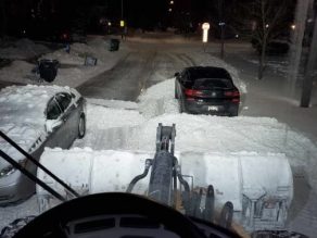 Photo taken at night on a Mississauga street from the perspective of a plow truck operator. Cars parked on the residential street prevent the plow from being able to safely and efficiently clear the snow on the road. 