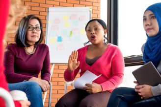 Three woman participating in a community meeting with a flip chart with post-it notes behind them