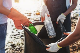 Close up of people putting trash in a black garbage bag during a park clean up