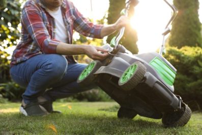 A person checks over a lawnmower on a sunny spring day.