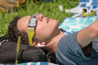 Person laying on the grass watching the total eclipse with eclipse glasses on