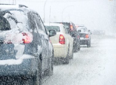 Snow-covered cars sit in traffic in the snow on a road.
