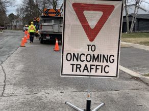City truck parked on a residential street during pothole repairs. A road sign reads: Yield to oncoming traffic. 
