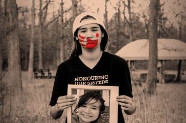 A child holds a photo of a young girl with a red handprint over his mouth.
