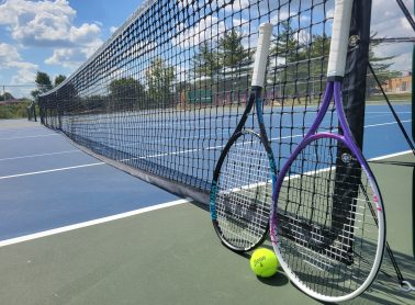 Two tennis racquets and a ball leaning against a tennis net