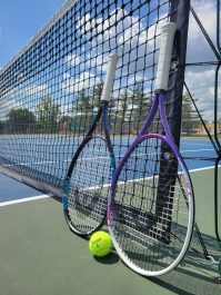 Two tennis racquets and a ball leaning up against a tennis net.
