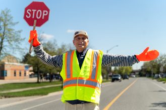 Crossing guard holding a stop sign with arms wide