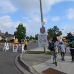 Photo: a closed road and pedestrians including school children and parents walking on the side walk.