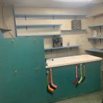 Work shop with blue shelving and a green counter with mini sticks hanging from it