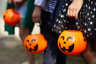 Close-up of children with pumpkins bags playing trick or treat outdoors.