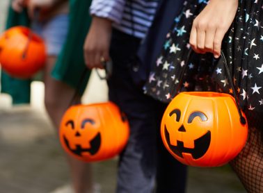 Close-up of children with pumpkins bags playing trick or treat outdoors.