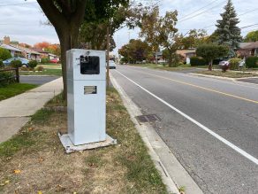 Speed camera placed on a sidewalk near a road. 