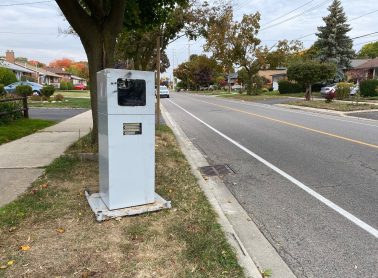 Speed camera placed on a sidewalk near a road.