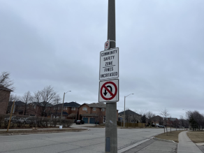 Sign mounted on a pole that reads Community Safety Zone. Fines increased