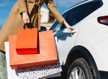 Person holding multiple shopping bags while opening a car door
