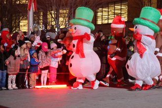 Kids enjoying Santa Claus parade with inflatable snowmen and gingerbreads walking the parade route
