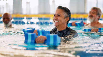 Close-up shot of a man smiling and swimming in a pool. He is holding water dumbbells.