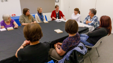 A group of people are seated around a rectangular table in a bright meeting room at a Mississauga library. They are engaged in discussion about a book.
