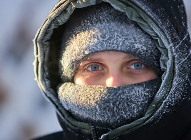 A full view a person wearing a hood with snow on it, braving the winter weather.
