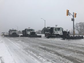 Three snow plows in a line clearing snow on road in Mississauga.